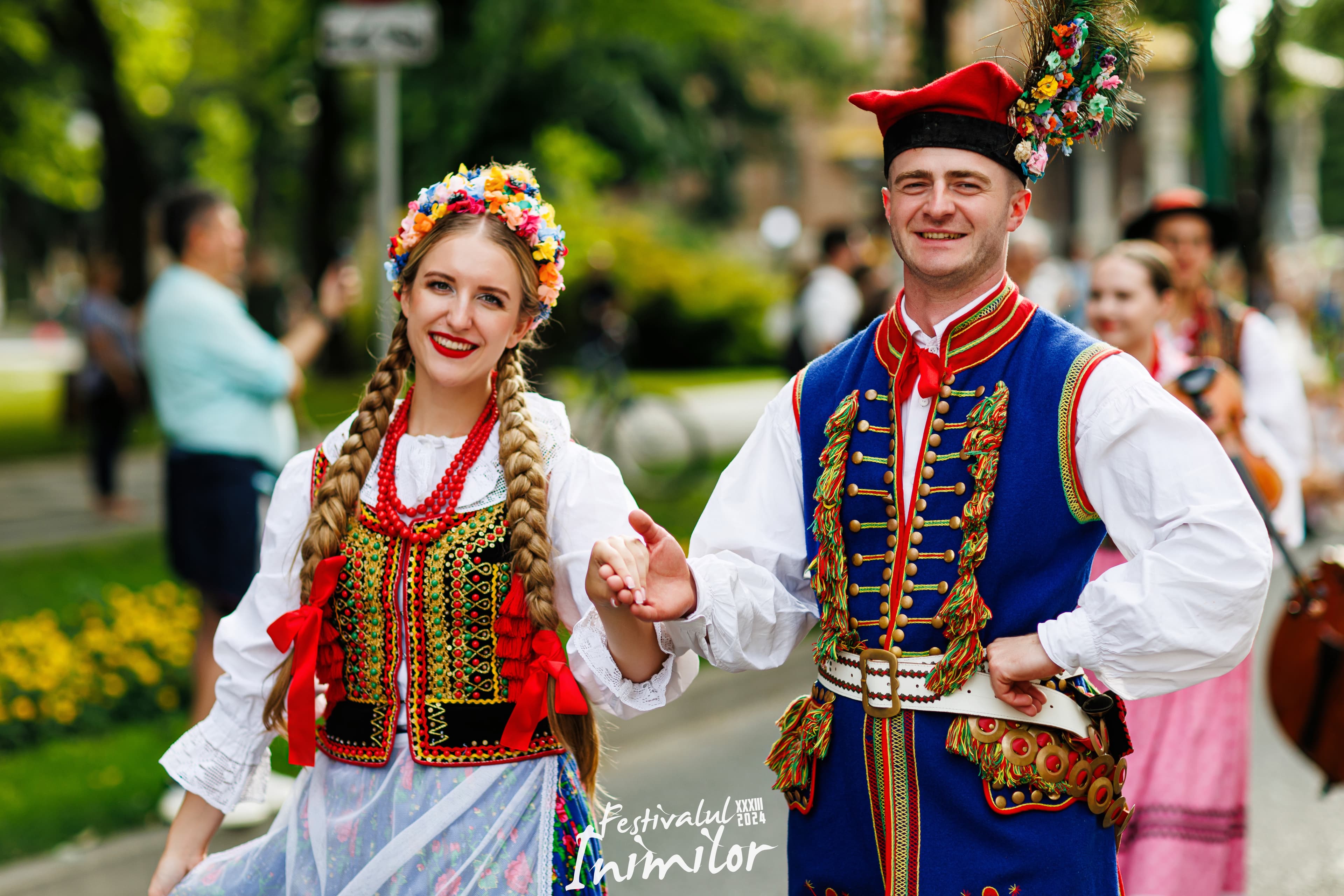 Cuplu polonez în port tradițional — el cu pălărie cu flori și vestă albastră, ea cu coroană florală